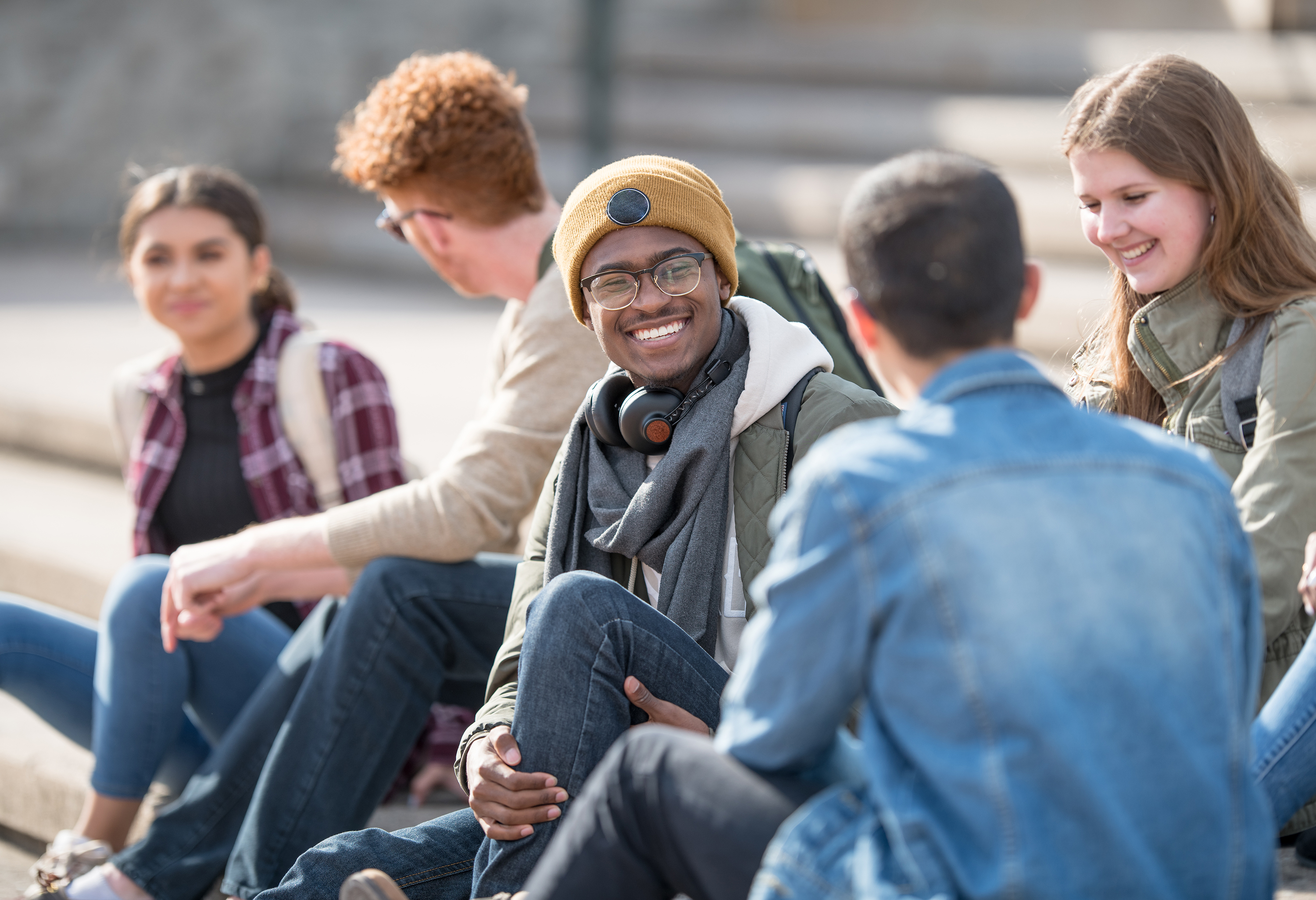 A group of students sit outside on stone steps, smiling and laughing.
