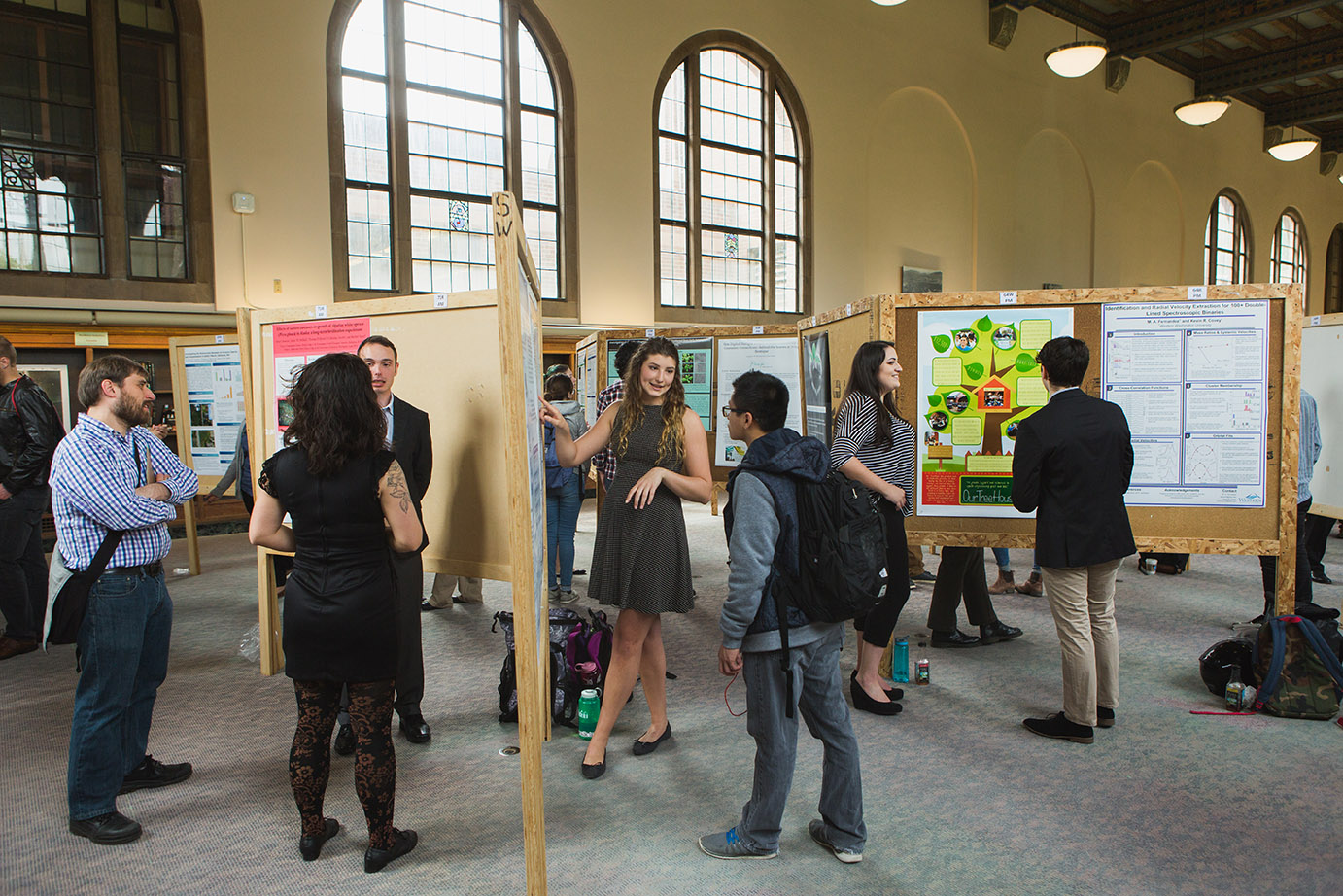 A woman stands in front of academic posters, explaining something to someone standing next to her.