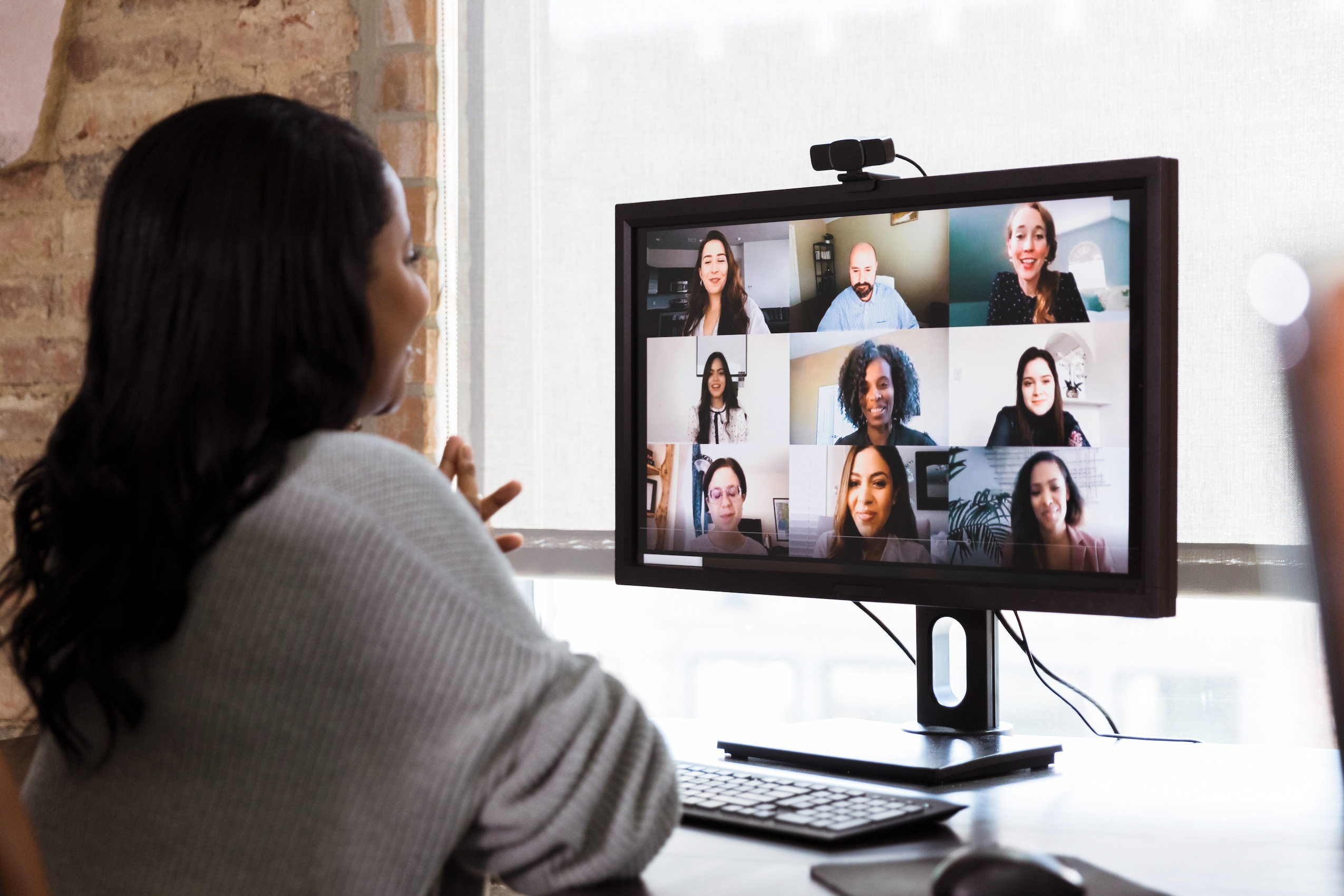 Picture of a woman at a desk, smiling while on a virtual conference with a diverse group of individuals. 