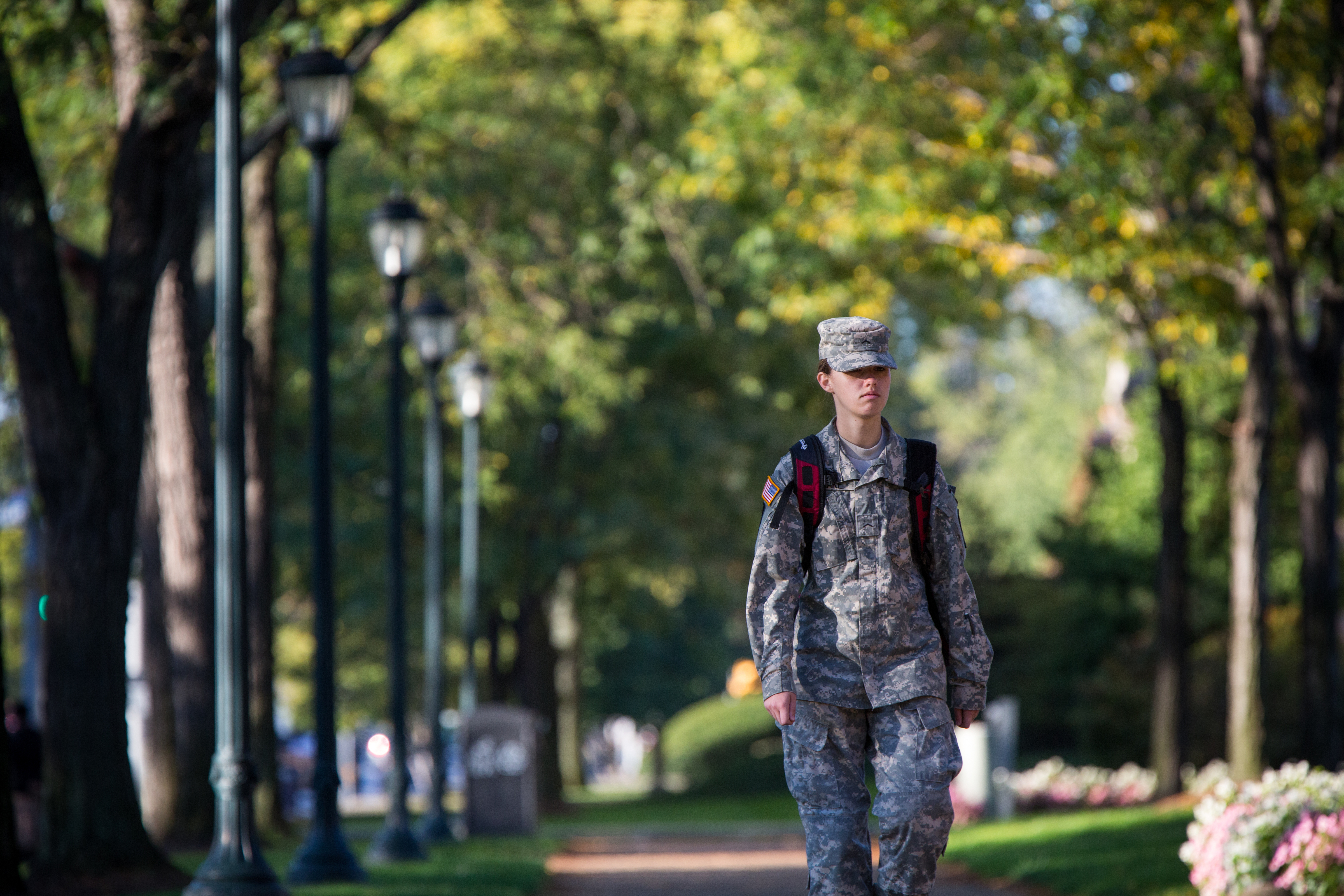 A military member walking along a campus sidewalk with a backpack on