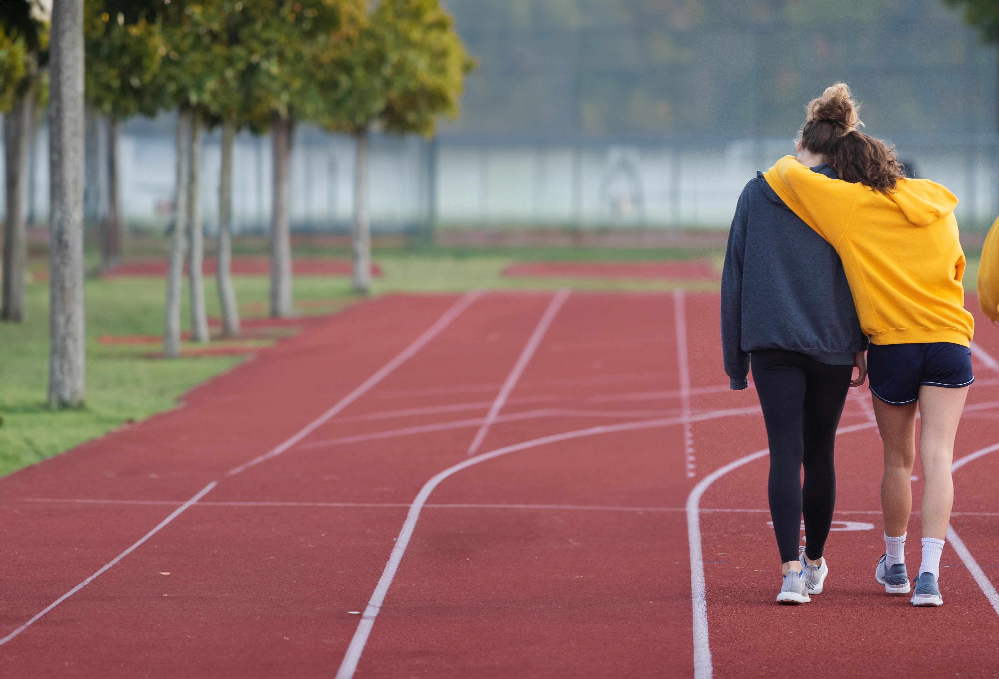 Two individuals stand on a track, holding each other in support while walking away from the camera.