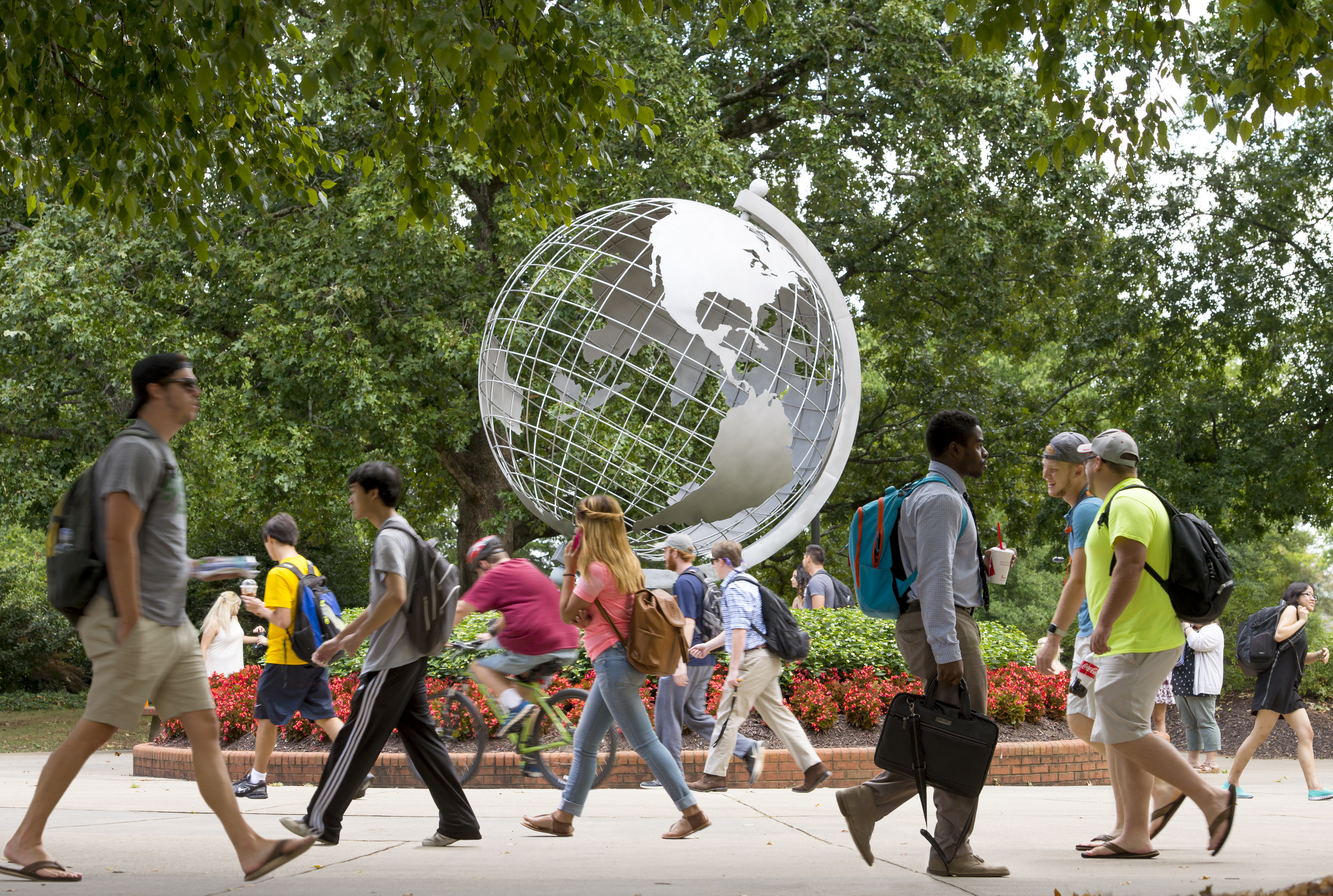 Picture of students on campus walking past a large statue of a globe. 