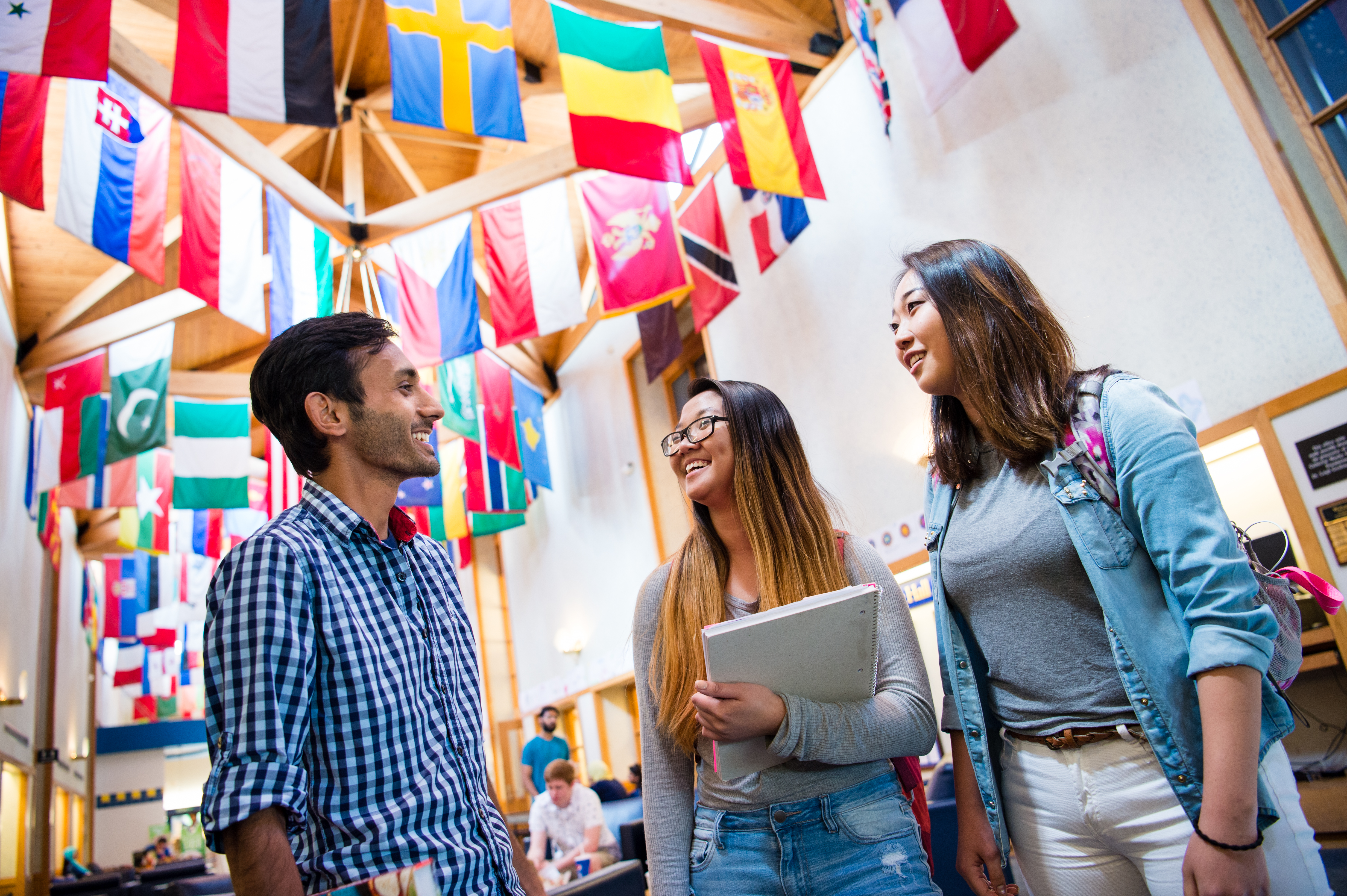 Picture of three students conversing below various hanging national flags