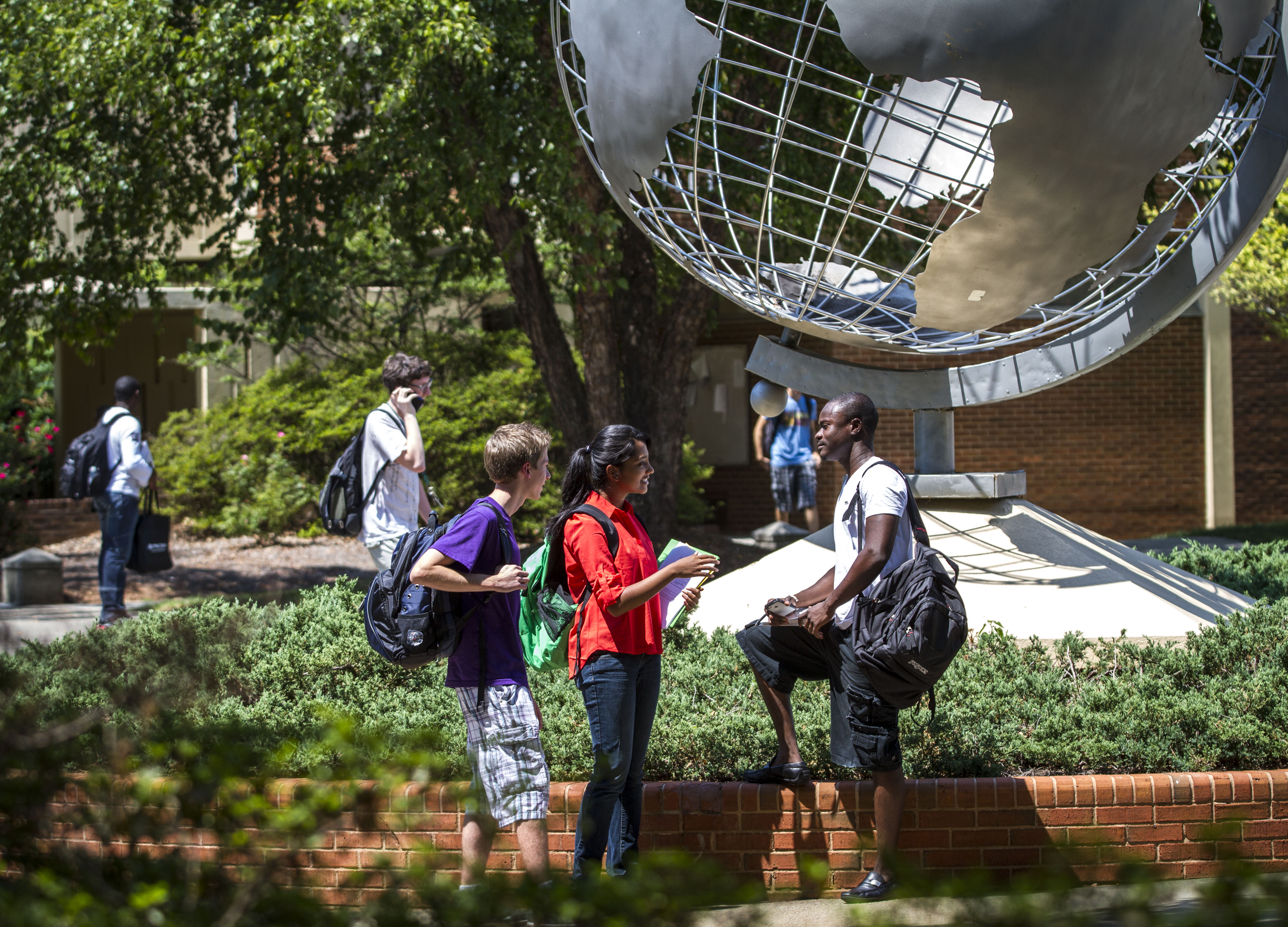 Picture of three students talking on campus in front of a globe.