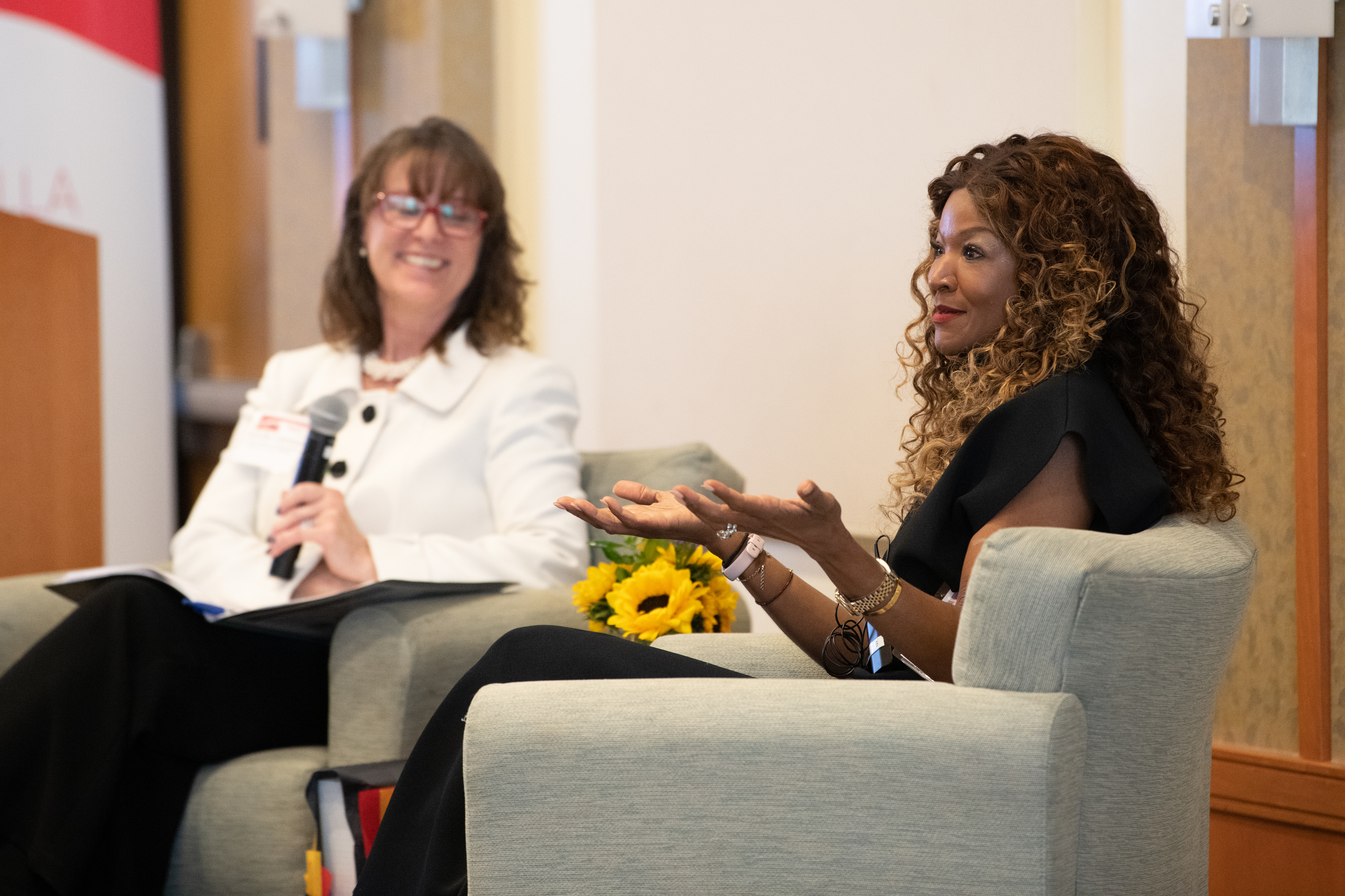 Photo of UMBrella founder and chair Jennifer Litchman sitting on a stage and interviewing UMB alum Tamika Tremaglio