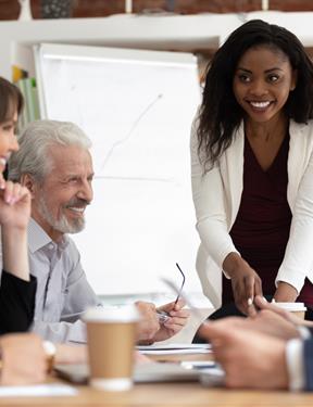 Photo of a professional woman addressing a group of smiling colleagues around a table