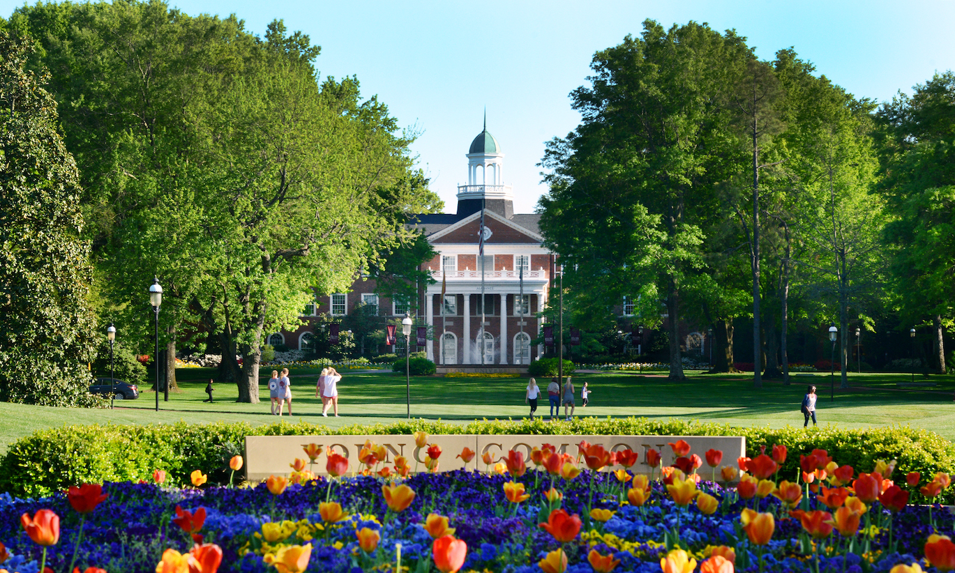 Photo of a campus building on a spring day with flowers blooming in front of it