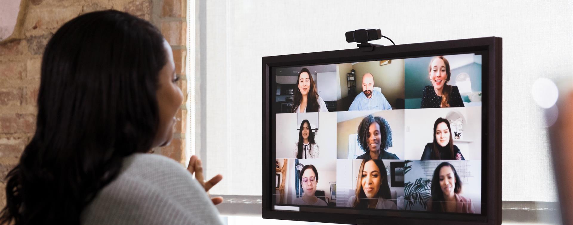 Picture of a woman at a desk, smiling while on a virtual conference with a diverse group of individuals. 
