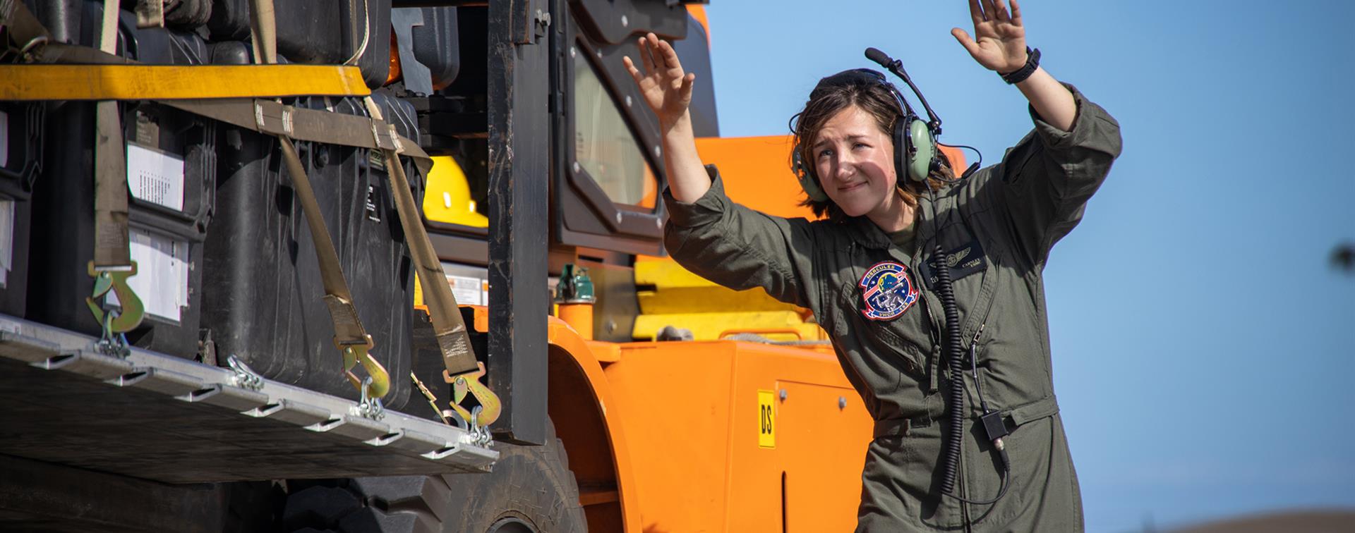 Photo of a woman in a jumpsuit standing beside and directing large construction equipment