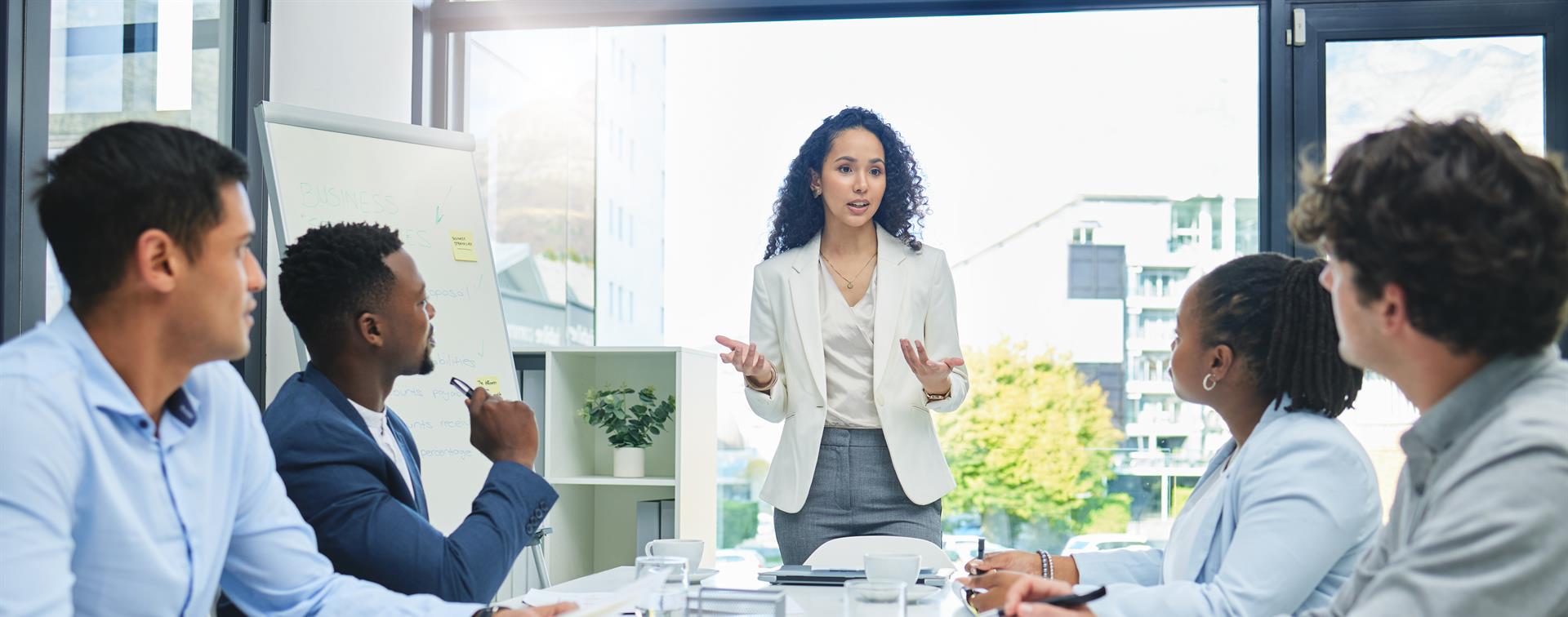 Photo of woman in a suit at the head of a table addressing a group in a modern conference room 