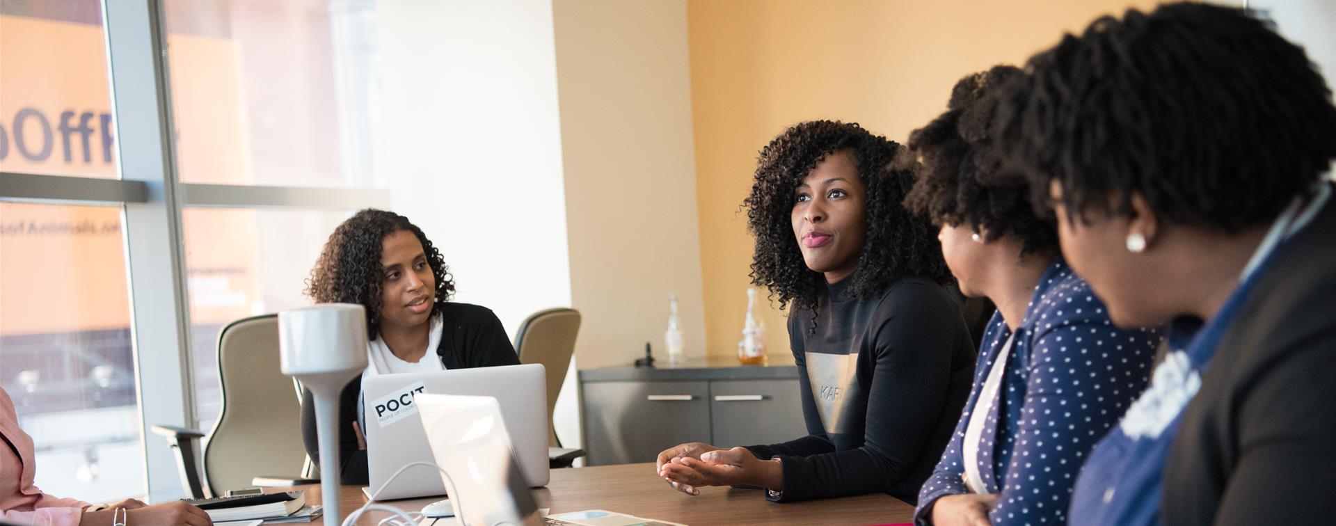 A group of people sit at table in a professional setting having a serious conversation.