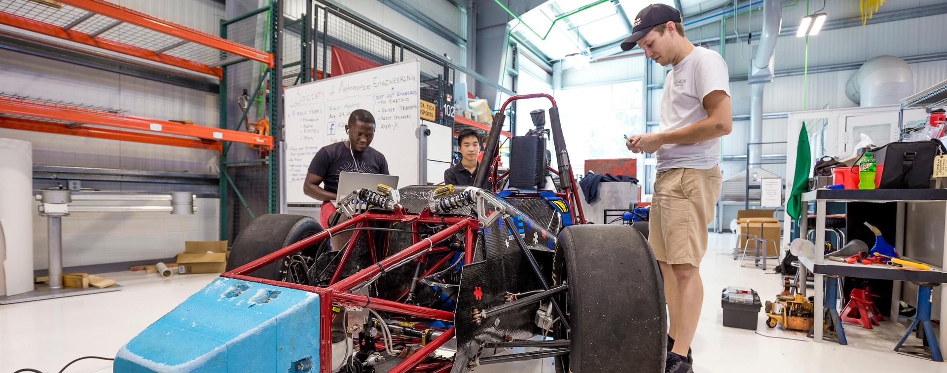 Photo of three students working on a vehicle in an automotive engineering workshop