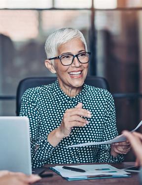 Photo of a professional woman smiling and talking with two others across her desk