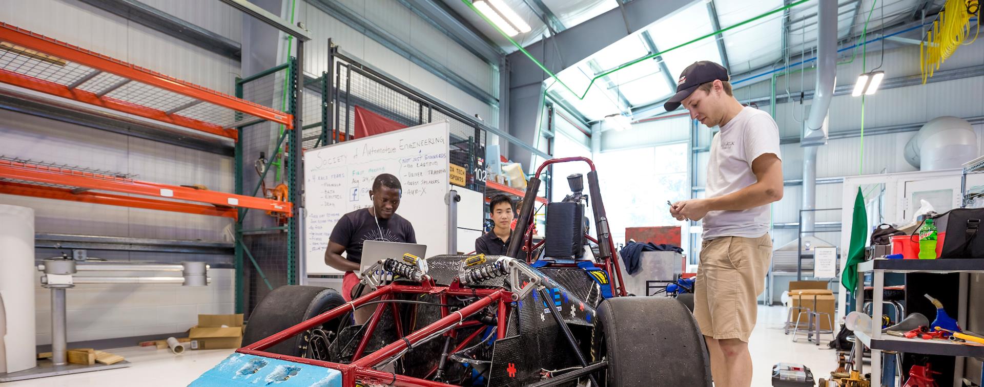 Photo of three students working on a vehicle in an automotive engineering workshop