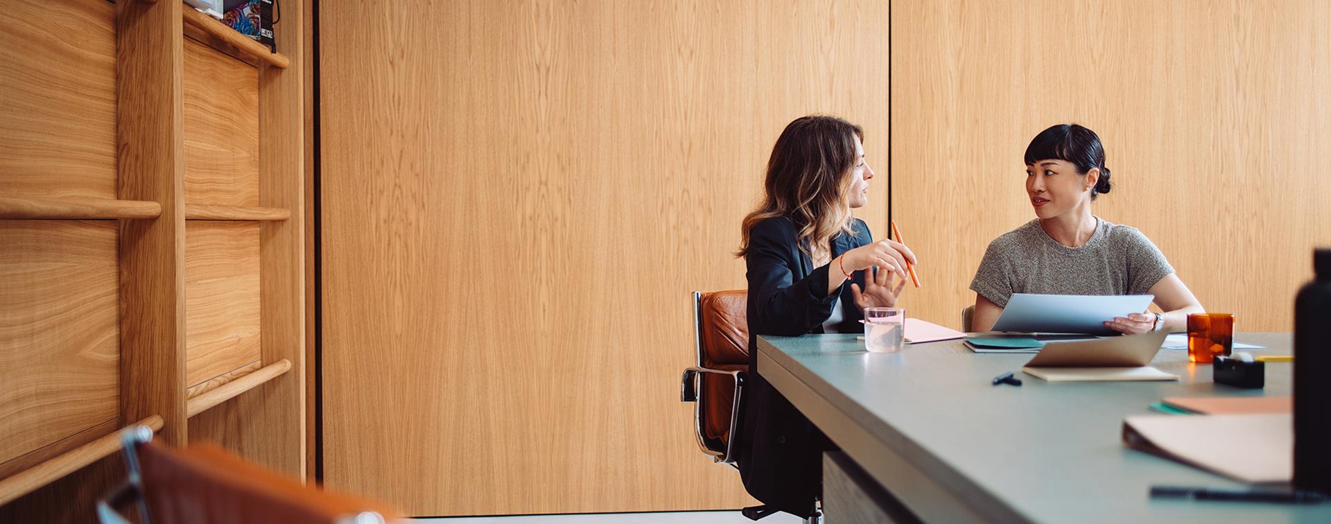 Photo of two women sitting at a table and having a conversation while looking at a paper doucment