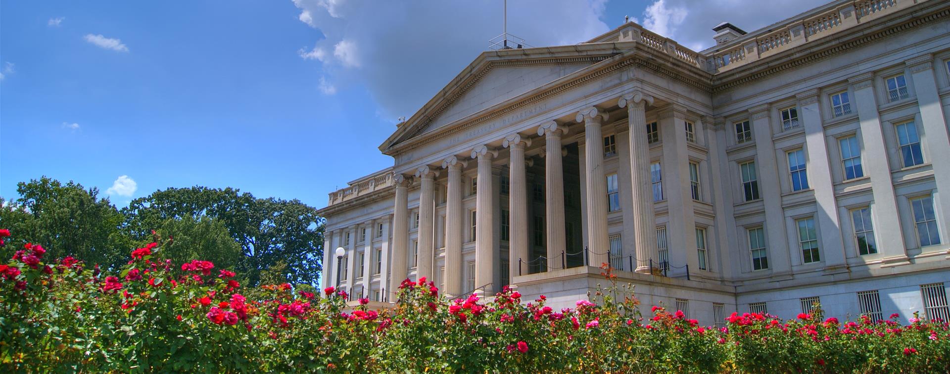 Picture of the US Treasury building with red flowers lining the bottom of the image.