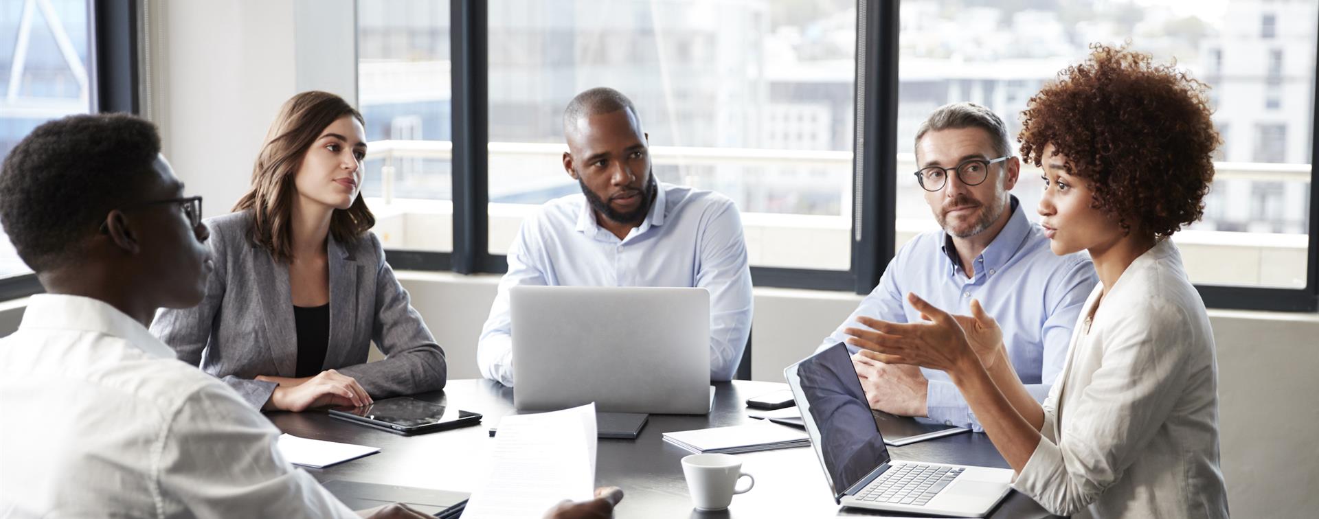 Picture of five individuals at a table, working together. 