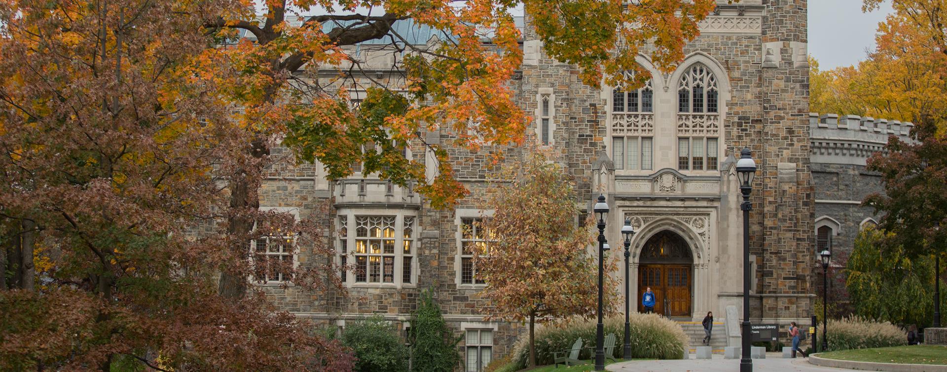 On old stone building is covered with fall foliage in front of it.