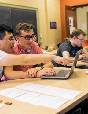 Two students from Gettysburg College sit in front of a laptop in a classroom, talking.