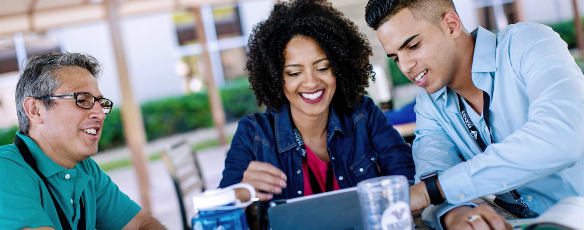 Three people gathered at a table and looking at a computer screen