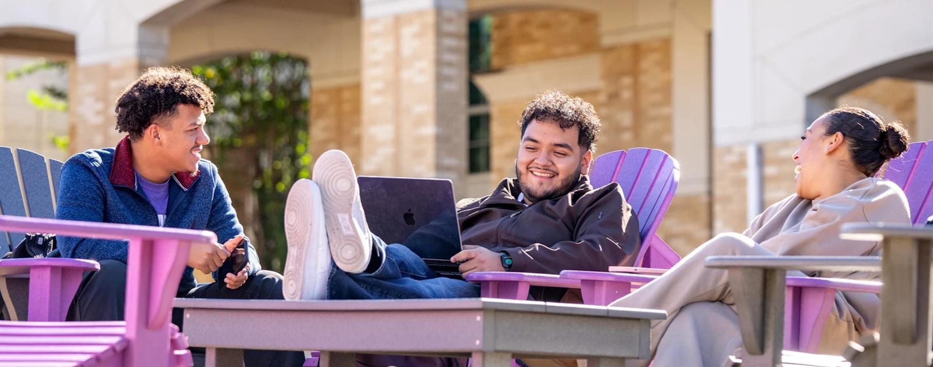 PHoto of three college students sitting in Adirondack chairs and chatting