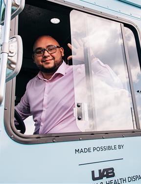 A man sits in a van smiling and waving. The van features "Healthsmart Alabama" text with a cartoon woman smiling.