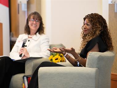 Photo of UMBrella founder and chair Jennifer Litchman sitting on a stage and interviewing UMB alum Tamika Tremaglio